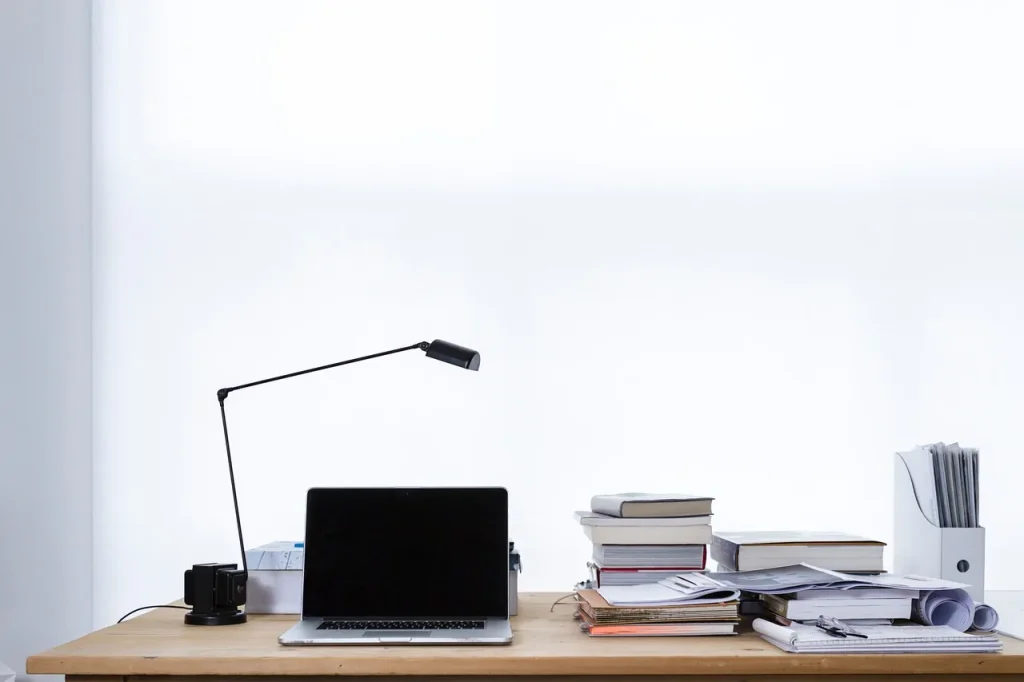 Bàn làm việc gọn gàng với laptop, đèn bàn và chồng sổ sách, minh hoạ việc ngồi chuẩn bị hồ sơ thuế