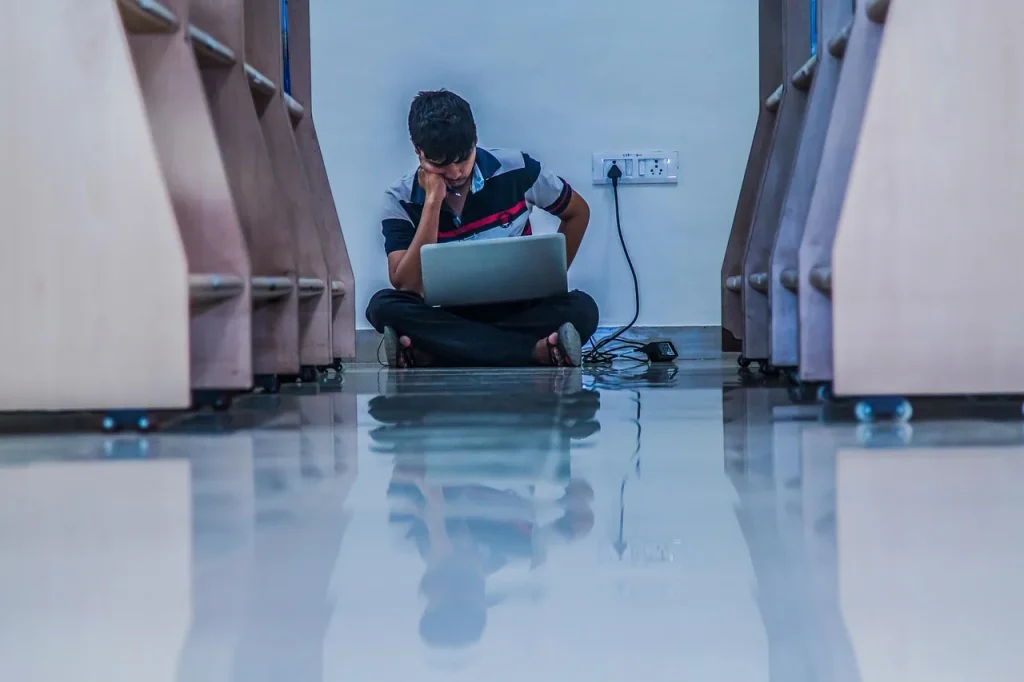 Một bạn trẻ ngồi sàn thư viện gập gối, đặt máy tính xách tay trên đùi, minh hoạ việc cân nhắc offer và chuẩn bị học ở Anh